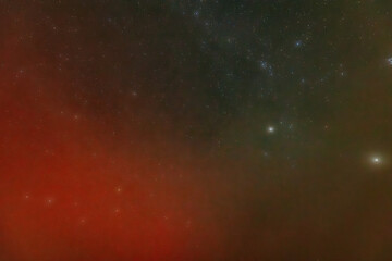 A peaceful night sky filled with faint stars and a soft red aurora glow near the horizon. The...