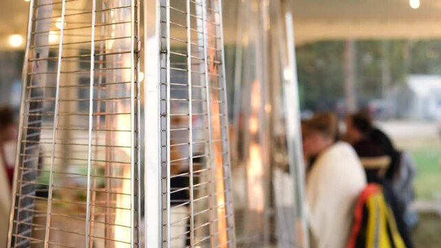 Slow motion captures a gas patio heater burning, creating a warm ambiance for diners in the background
