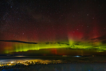 A vivid aurora borealis with striking red and green hues lights up the starry night sky above a...