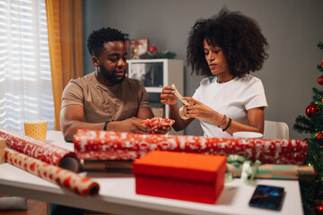 Joyful african american couple enjoys gift wrapping in a festive setting.