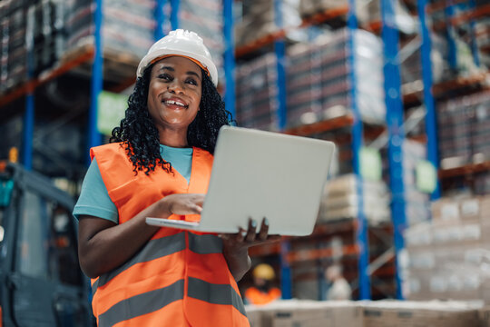 Smiling warehouse worker using laptop for inventory management