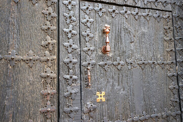 Antique wooden gate decorated with nailed wrought iron and metal knocker.