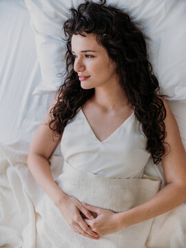 Beautiful Curly Haired Young Woman Relaxing in Bed at Home