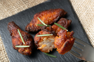 Close-up of crispy, golden-brown fried chicken wings garnished with fresh rosemary sprigs. A piece of chicken is held on a fork, highlighting its texture and juiciness.