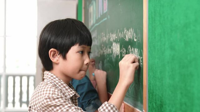 Side view of asian boy writing engineering prompt and programing system while standing blackboard with generated AI prompt written by attractive student at STEM technology lesson. Closeup. Pedagogy.