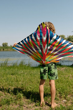 A barefoot Child Holding a Vibrant Kite by the Rive on a Sunny Day