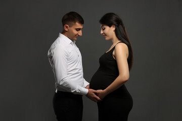 Beautiful pregnant woman with her husband on grey background