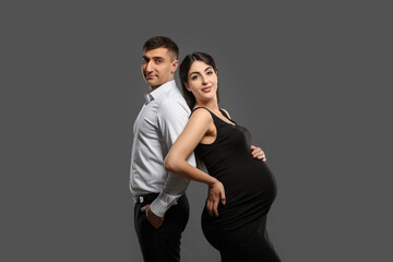 Beautiful pregnant woman with her husband on grey background