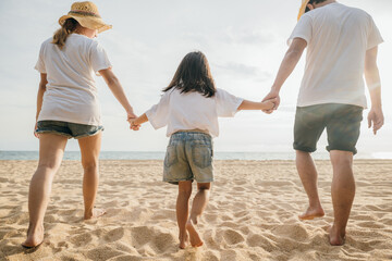 Happy Asian parents with their daughters enjoying playful at beach. Little girls with their mother and father holding hand of child walking on sand beach. Positive family outdoor activity