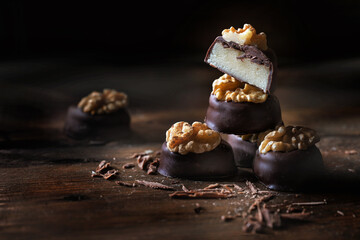 Marzipan pralines with a dark chocolate coating and a walnut garnish, whole and halved, stacked on rustic dark wooden planks, holiday sweets, copy space, selected focus