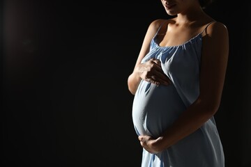 Pregnant woman on black background, closeup. Space for text