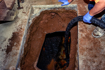 Worker decommissions an underground residential oil tank with a suction hose to extract thick oil...