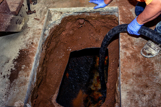 Worker decommissions an underground residential oil tank with a suction hose to extract thick oil sludge from a tank that's partially dug out for access. Hazardous material oil sediment removal work.