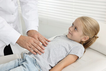 Fototapeta premium Doctor examining little girl with stomach pain in hospital, closeup