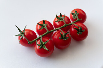 A close-up of a branch with seven cherry tomatoes on a white background. Bright red, ripe cherry...
