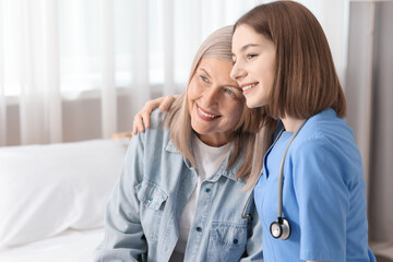 Smiling healthcare worker supporting senior patient on bed indoors. Space for text