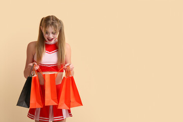 Young woman dressed for Halloween as cheerleader with gift bags on beige background