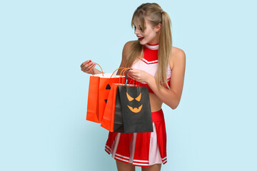 Young woman dressed for Halloween as cheerleader with gift bags on blue background