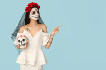 Young woman dressed as dead bride for Halloween party with painted human skull pointing at...