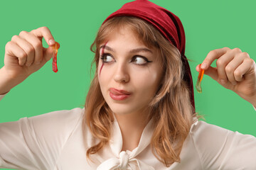 Young woman dressed for Halloween as pirate with jelly worms on green background, closeup