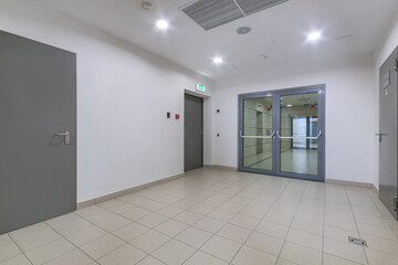 The floor of a modern office building with a light decor. Grey doors and a double-leaf .glass door.