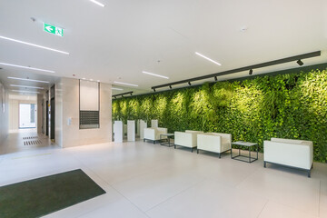 Exclusive design of the lobby of the office center. White armchairs and tables against .the wall decorated with green plants.