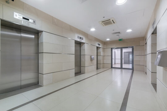 Spacious lobby in an office building. Modern elevators with metal doors. The room is .decorated with light tiles.