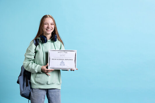 Cheerful teenager holding school award, excited after receiving accreditation for passing classes. Jolly person grateful for received honor, isolated over studio background