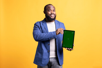 Cheerful african american man recommending isolated screen tablet, isolated over studio background. Joyous BIPOC person presenting chroma key device, giving positive feedback