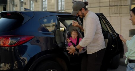 A confident brunette man with a beard in a white shirt takes out his little daughter in a pink dress and goes with his wife