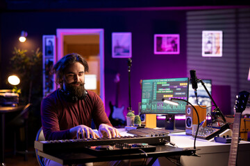 Fototapeta premium Modern artist playing piano notes to record a new soundtrack, trying to compose a song using midi controller electronic keyboard. Singer composer playing instrument keys to create songs.
