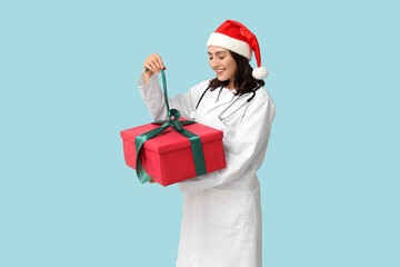 Beautiful female doctor in Santa hat with gift box on blue background