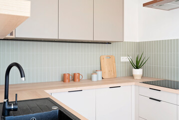 Fototapeta premium Modern kitchen interior with kitchen sink with faucet, green tiles on the wall and white beige furniture in stylish design. Simplicity and fashionable style at home. Real estate.