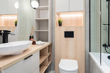 Luxury bathroom with glass to shower, round mirror with led lights, stylish washbasin on wooden cabinet. Modern interior of bathroom with wc and bath.	