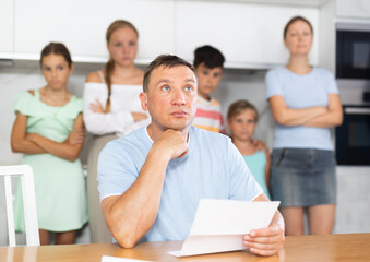 Obraz premium Upset father reads and looks through financial documents. Sad wife with children in the background