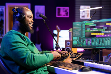 Skilled audio engineer working with mixing console in home studio, producing new soundtracks for a...