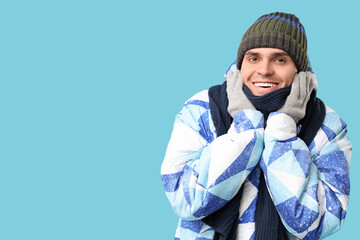 Young man in stylish puffer jacket and scarf on blue background