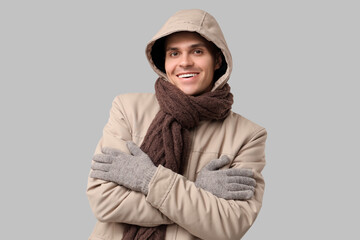 Young man in stylish puffer jacket and scarf on grey background
