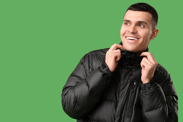 Young man in black stylish puffer jacket on green background