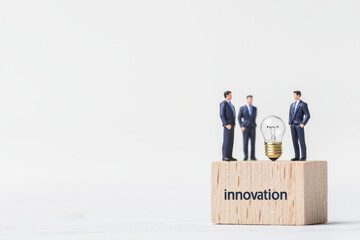 Miniature businessmen discussing innovation with a lightbulb concept, isolated on white background.