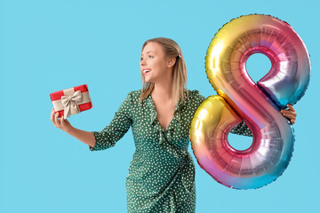 Young woman with hearing aid holding balloon in shape of figure 8 and gift on blue background. International Women's Day