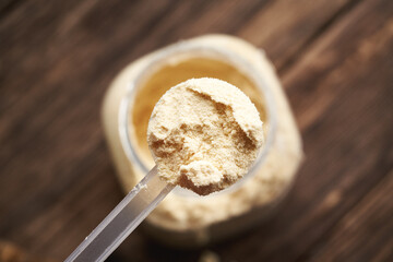 Whey protein powder in a measuring spoon above a jar