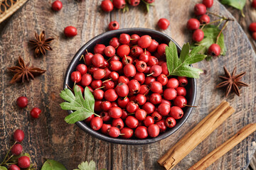 Fresh hawthorn berries harvested in autumn in a black bowl on a wooden table, top view