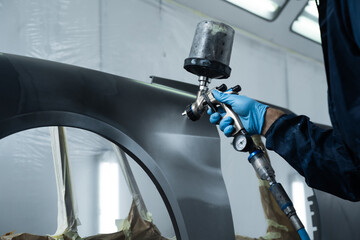 Car painter is painting car hood in dark color. Mechanic is fixing color of car with paint sprayer...