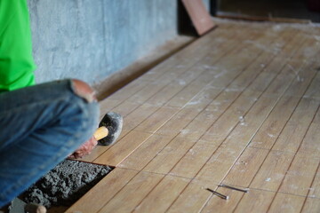 Professional tiling technicians lay floor tiles on the cement surface of the room.