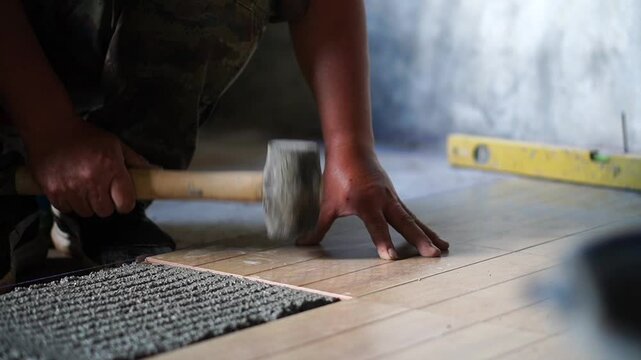 Professional tiling technicians lay floor tiles on the cement surface of the room.