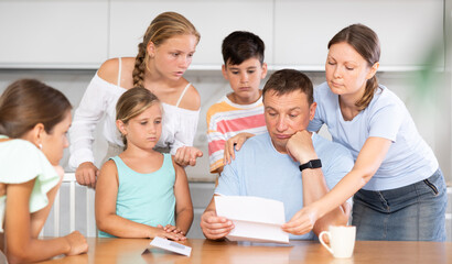 Loving wife with children comfort upset man at home table