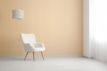 Comfortable armchair and lamp near beige wall