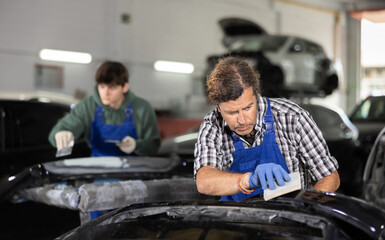 Man prepares car for painting in workshop - grinds and puts putty on the bumper before painting