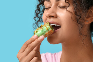 African-American woman eating tasty eclair on blue background